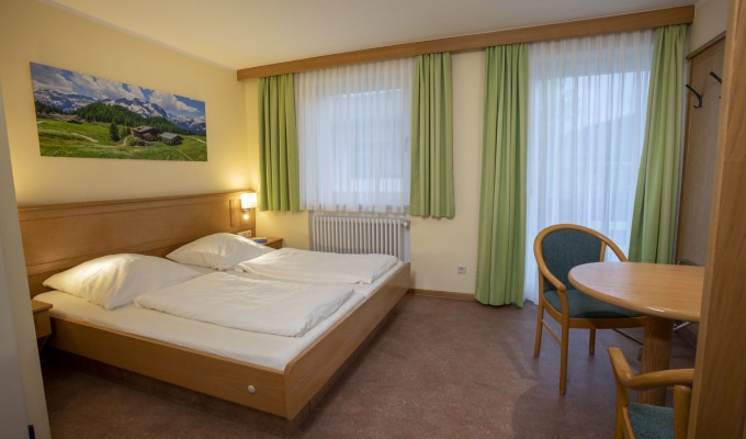 Helles Doppelzimmer im Haus Chiemgau mit Balkon, Tisch und Stuhl – gemütlich und funktional eingerichtet.