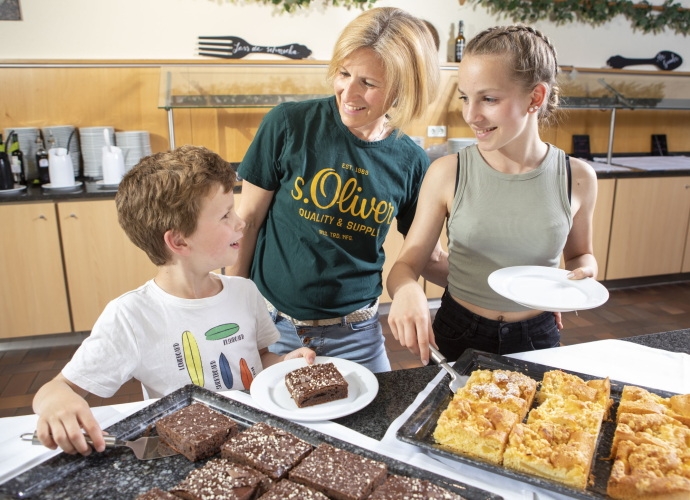 Frau mit zwei Kindern am Buffet die sich Kuchen holen.