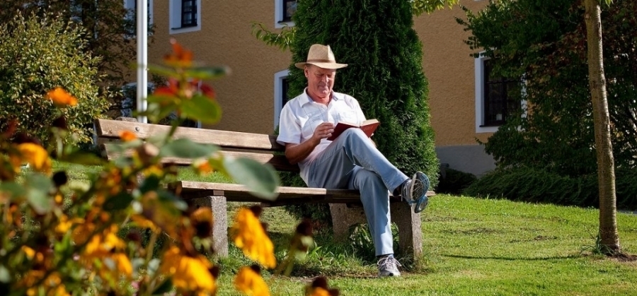 Ein Mann der auf einer Bank im Garten vom Haus Chiemgau sitzt und entspannt ein Buch ließt